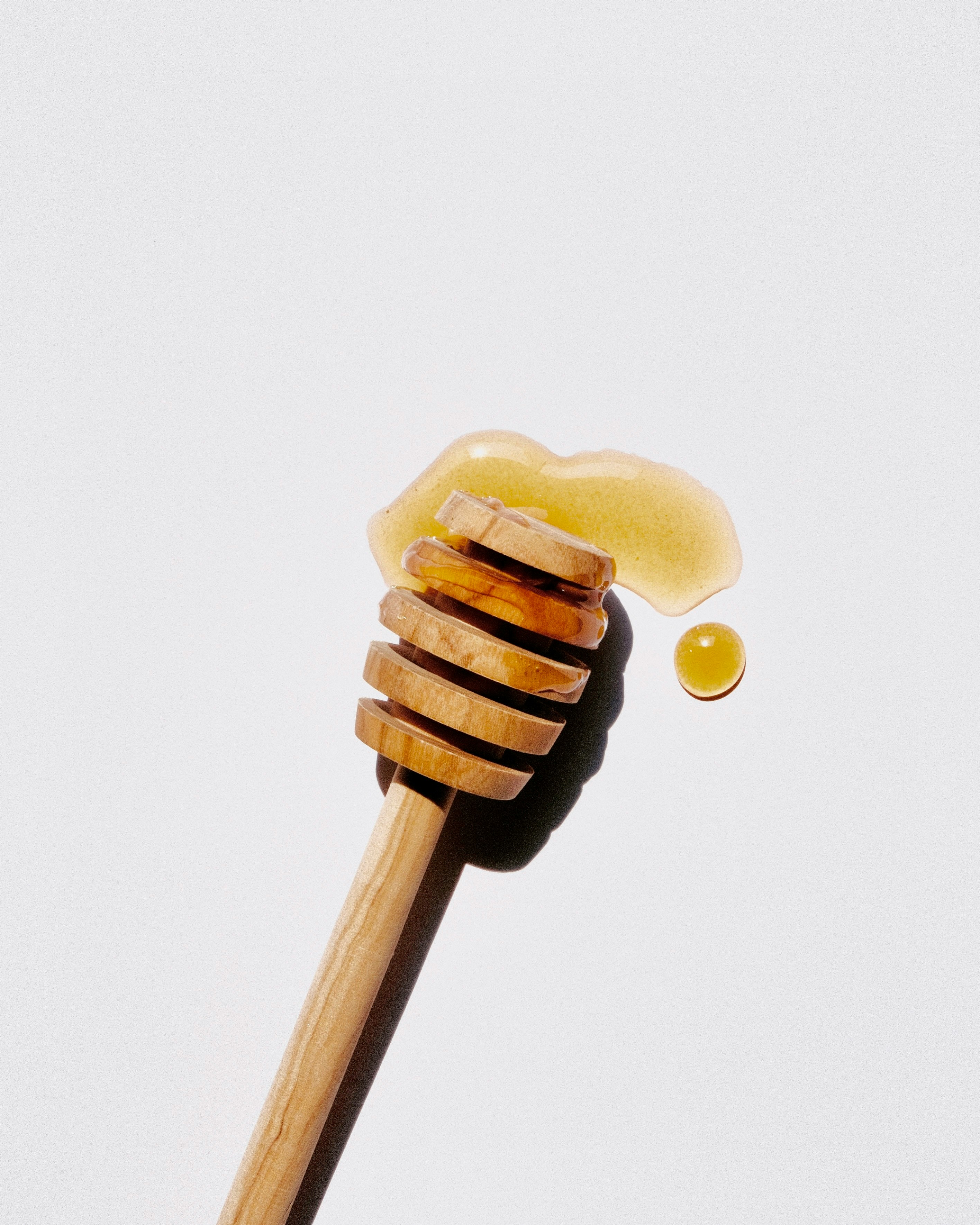 A wooden honey dipper dripping raw manuka honey.